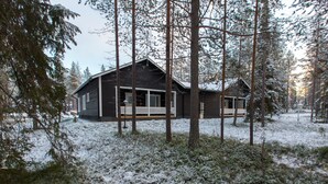 A two-story cabin with a porch, surrounded by tall trees and covered in snow. - Pihkala 2 by Interhome (Äkäslompolo)