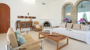 Sala de estar com sofá, poltrona, mesa de centro de madeira, lareira e arcos de pedra.
