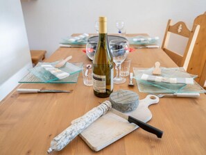 Une table de salle à manger en bois, avec une bouteille de vin, des verres et des couverts.