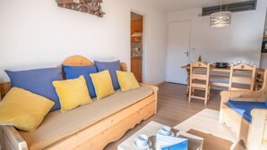 Una habitación acogedora con un sofá de madera, una mesita con un libro y tazas, y un comedor con sillas y una mesa de madera.