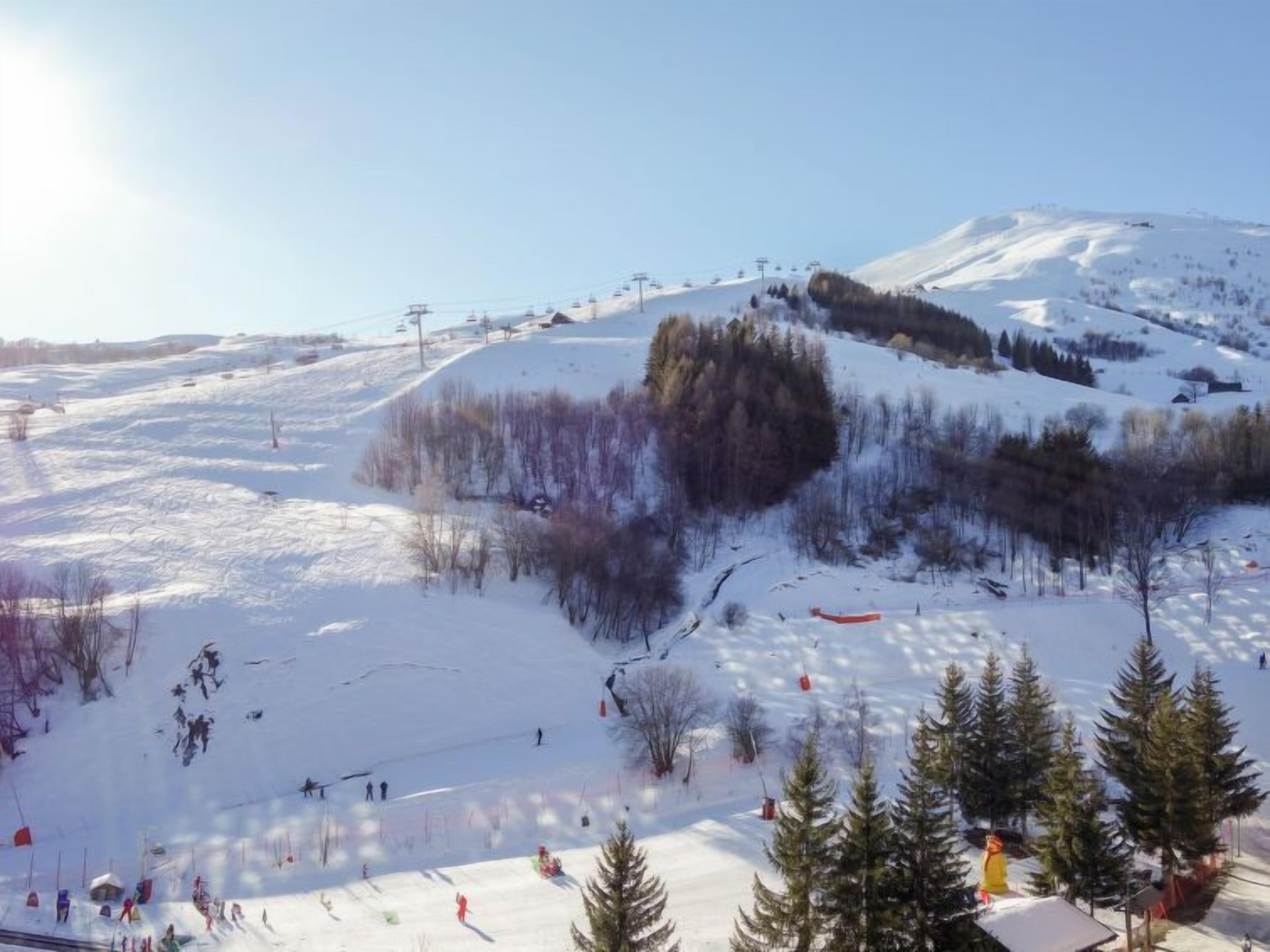 Ein verschneiter Skipisten mit Seilbahn und Bäumen im Hintergrund.