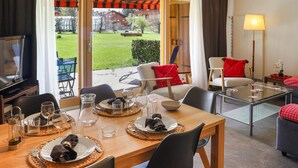 Un comedor con una mesa dispuesta para cuatro personas, un televisor y vistas a un jardín y edificios.