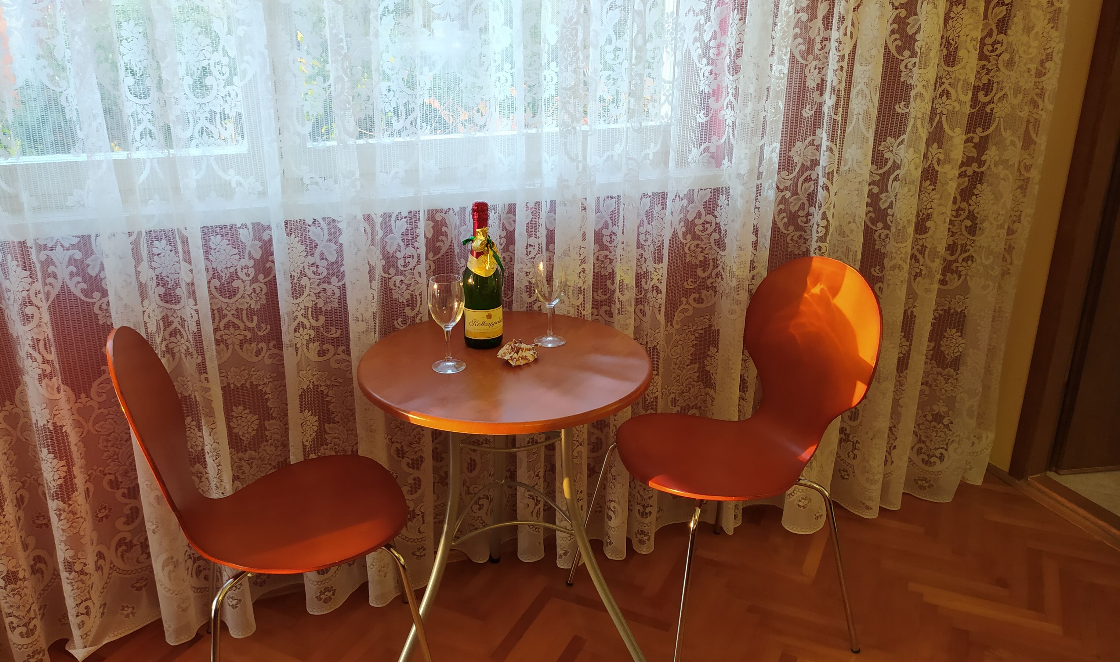 A small round table with two orange chairs, a bottle of champagne, and two glasses.