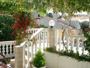 Une balustrade blanche agrémentée d’un luminaire sphérique, d’une plante en pot et de fleurs rouges.
