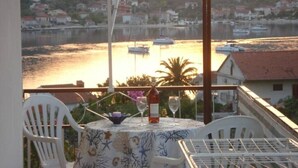 Un balcon avec une table dressée pour deux personnes, donnant sur une étendue d’eau où naviguent des bateaux, et sur une ville perchée sur une colline en arrière-plan.
