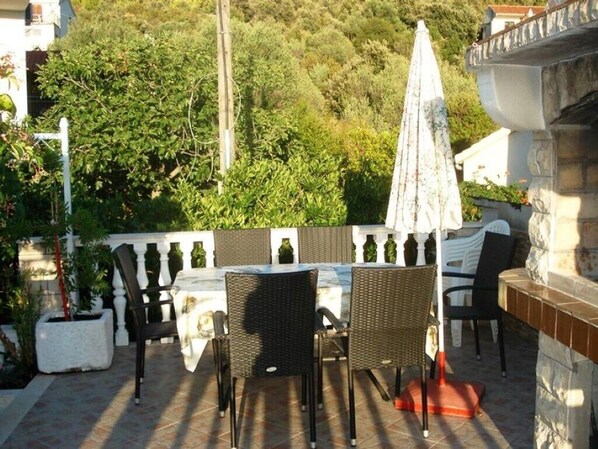 An outdoor patio with wicker furniture, a table, and a white umbrella. - Romantic apartment with sea view Vinišće, Dalmatia (Vinišće)