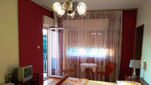 Une chambre d’hôtel comprenant un lit, un bureau avec une télévision, une chaise, une petite table et une fenêtre avec des rideaux.