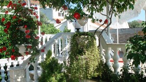 Une balustrade blanche ornée de fleurs rouges, un arbuste vert et un mur blanc.