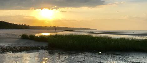 A beach with a sunset, wet sand, and distant shoreline.