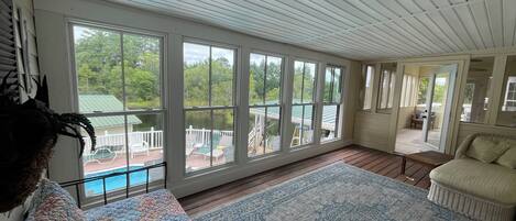 A spacious room with large windows, a wooden floor, and a view of a deck and pool.