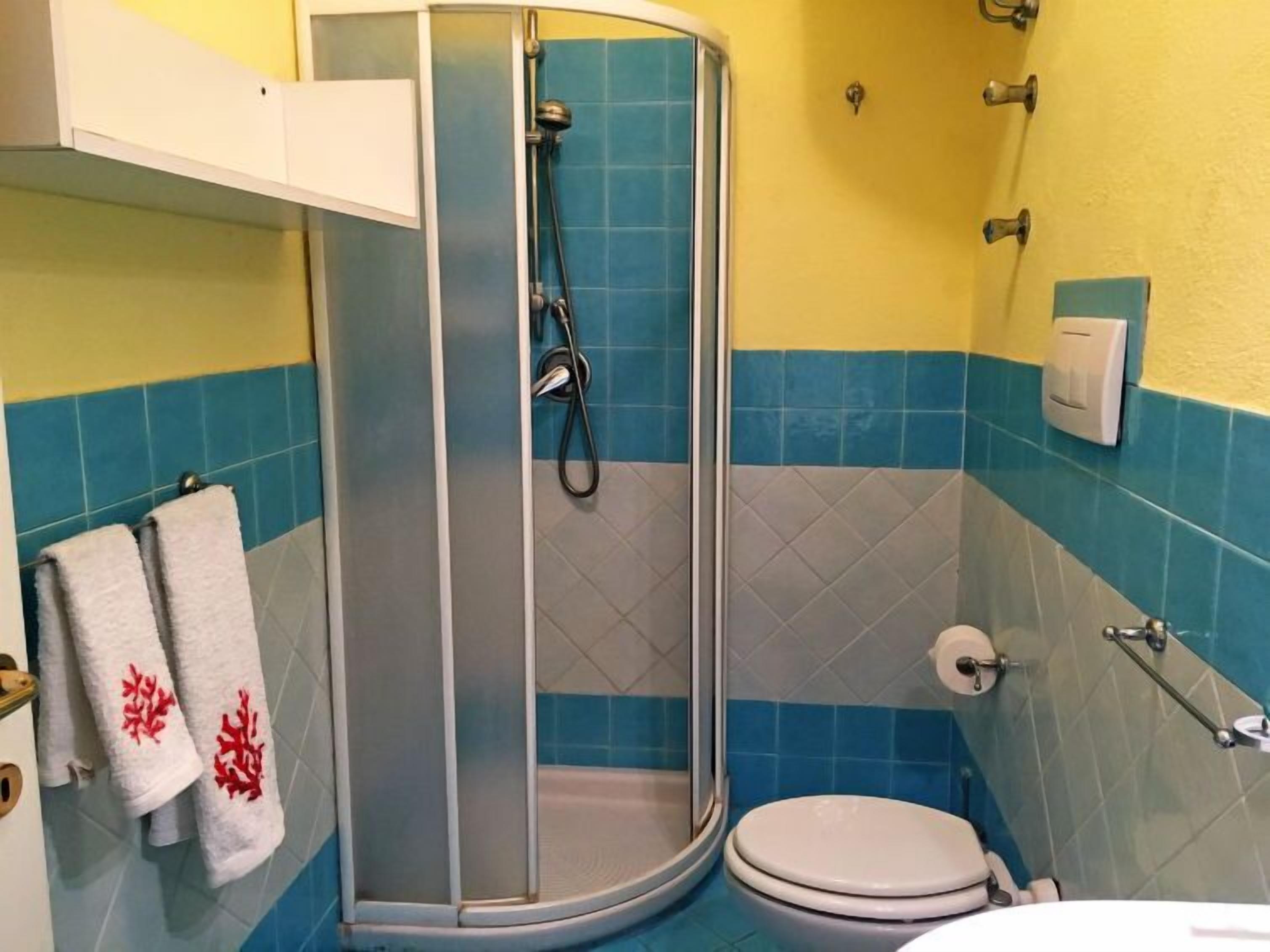 A bathroom with a glass-enclosed shower, a toilet, and a towel rack with towels.
