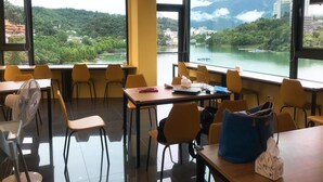 A dining area with tables and chairs, large windows with a view of a lake and mountains, and a ceiling fan.