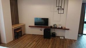 A modern living room with a flat-screen TV mounted on a wooden shelf, a coffee machine, and a speaker on the floor.
