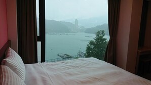 A hotel room with a large window overlooking a body of water, a bed, and curtains.