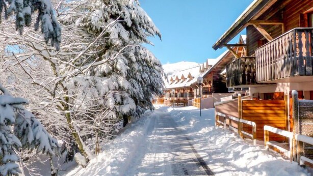 A snow-covered wooden building with a balcony, a clear sky, and a snow-covered path.