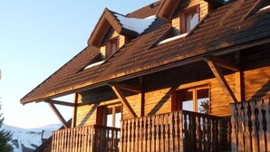 A wooden chalet with a balcony and a sloped roof covered in snow.