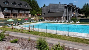 A swimming pool with lounge chairs and umbrellas, surrounded by wooden buildings with balconies.