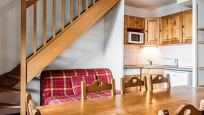 A wooden staircase leading to a dining area with a wooden table and chairs, a red plaid sofa, and wooden cabinets in the background.