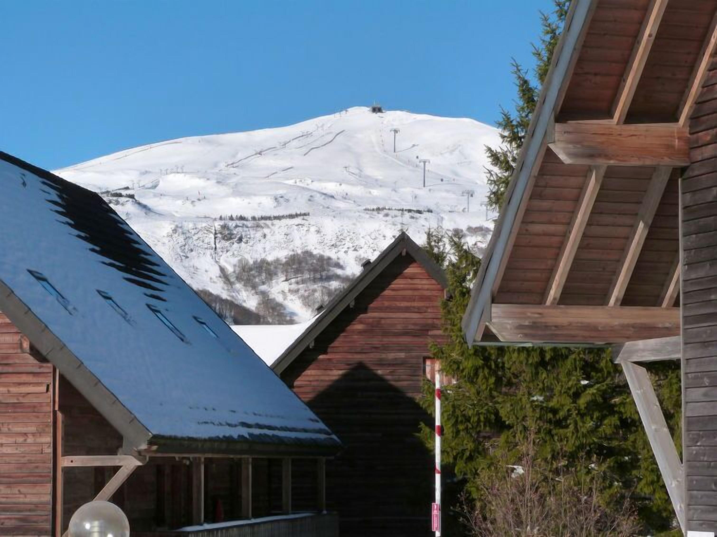 Une cabane en bois avec un toit enneigé, une vue dégagée sur une montagne aux sommets enneigés et une terrasse en bois.