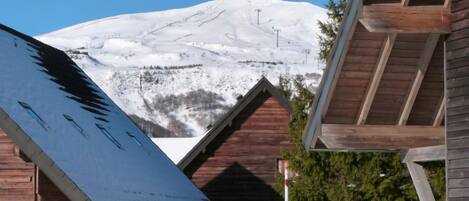 Une cabane en bois avec un toit enneigé, une vue dégagée sur une montagne aux sommets enneigés et une terrasse en bois.
