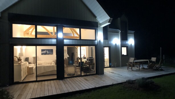 Una casa moderna con amplios ventanales, una terraza de madera y un comedor con mobiliario exterior.