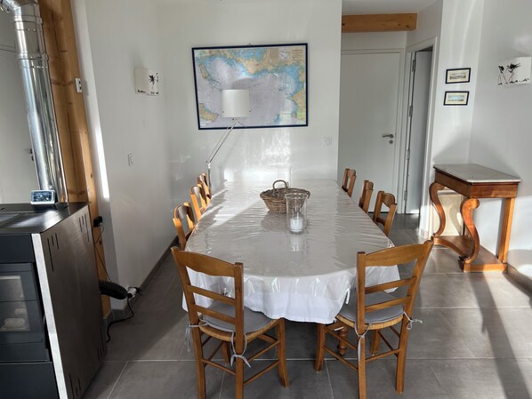 Un comedor con una mesa larga, sillas de madera, un mapa en la pared y una mesita con una lámpara.