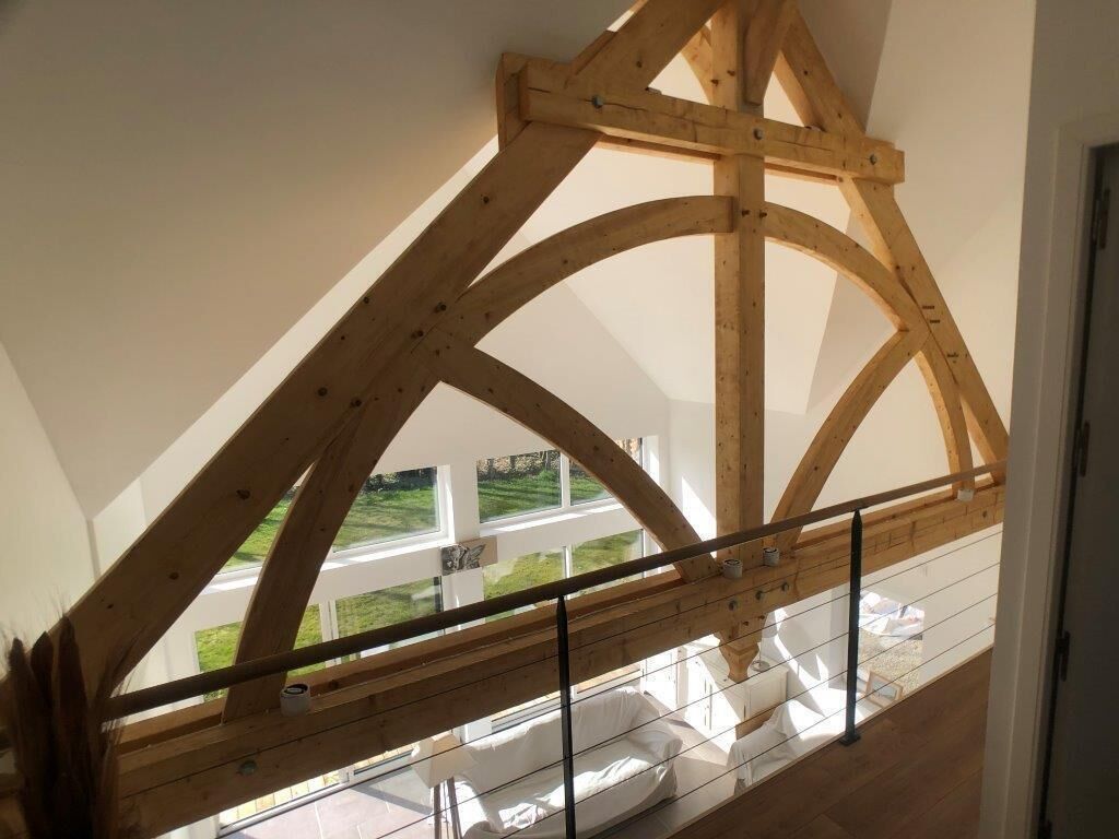 Una habitación con techo de vigas de madera, un balcón de cristal y vistas a un paisaje verde.