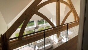 Una habitación con techo de vigas de madera, un balcón de cristal y vistas a un paisaje verde.