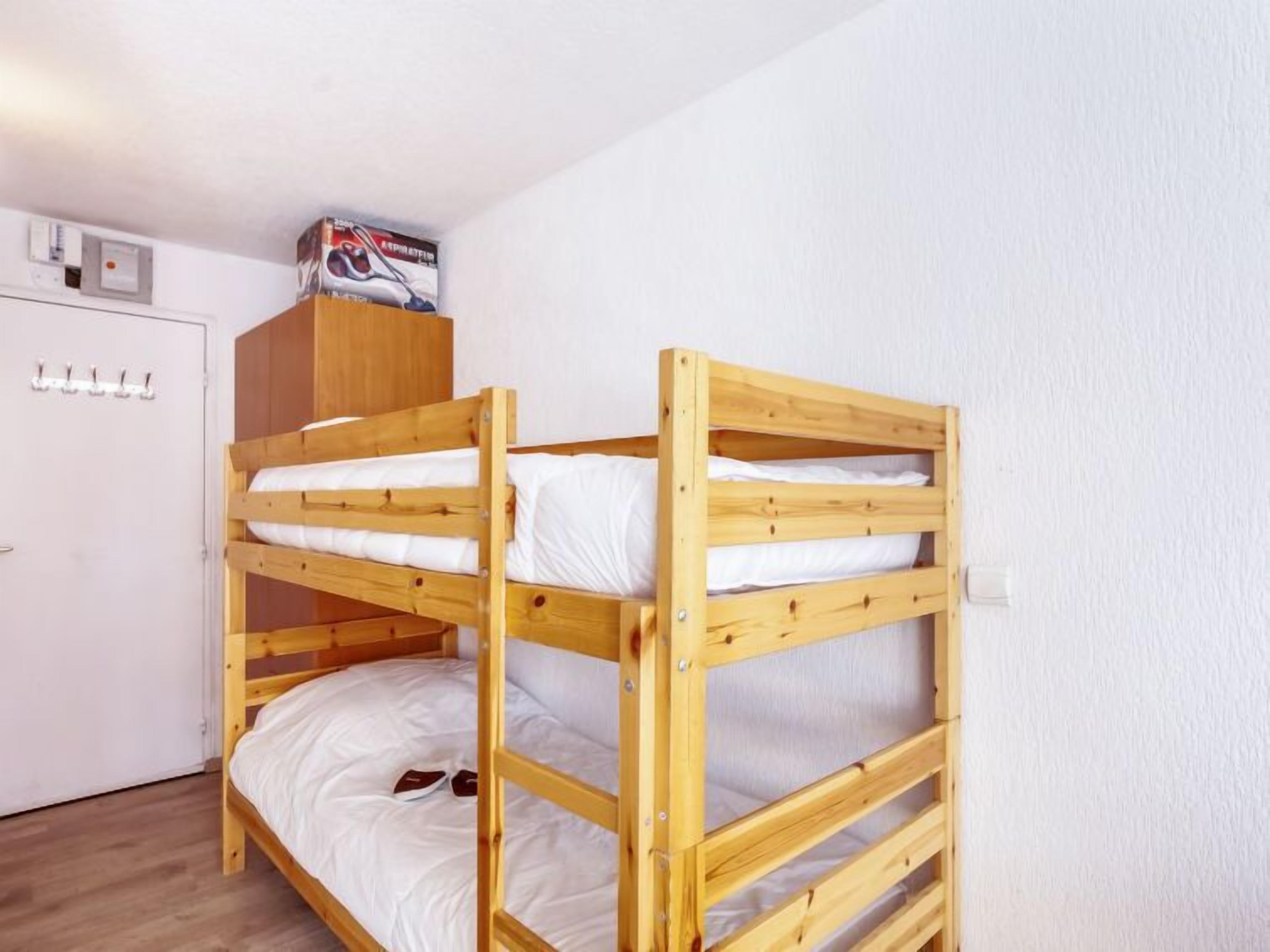 Une chambre avec un lit superposé, une tête de lit en bois, une porte blanche avec des crochets et un petit placard au-dessus du lit.