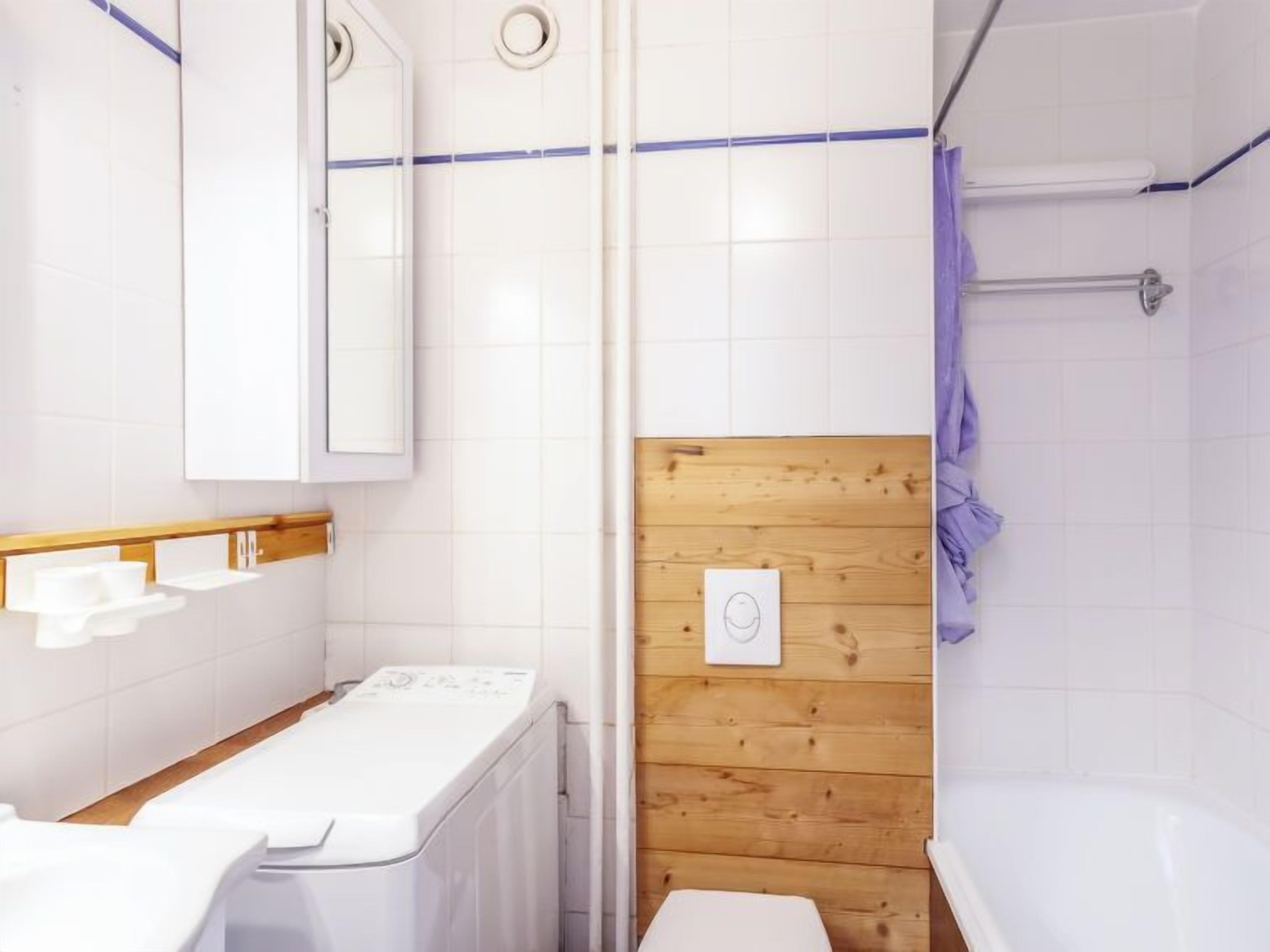 A modern bathroom with a wooden panel wall, a white sink, a toilet, and a bathtub.
