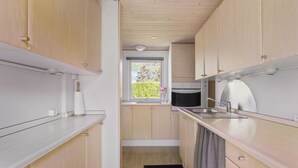 Cocina compacta con muebles de madera, un lavamanos de acero inoxidable y una ventana con vistas a la vegetación.