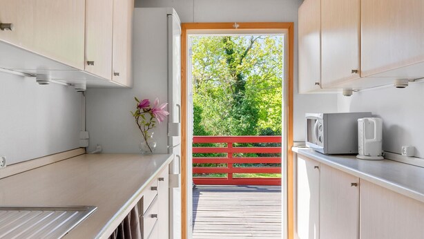 Una cocina compacta con una puerta de madera que da a un balcón, un microondas y un lavamanos pequeño.