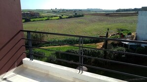 Ein Balkon mit Metallgeländer, der auf eine ländliche Landschaft mit Feldern und weit entfernten Gebäuden blickt.