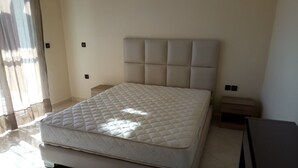 Ein Schlafzimmer mit einem großen Bett, einem Nachttisch, einer Kommode und einem Fenster mit Vorhängen.