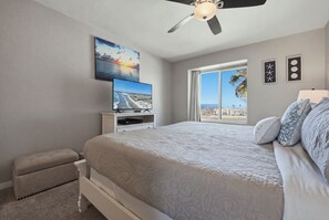 A bedroom with a bed, a television, a ceiling fan, a window with a view, and a small table. - 2 Story Condo- Panoramic Ocean Views- F311 North Coast Village (Oceanside)
