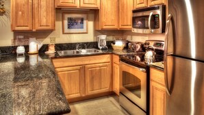A kitchen with wooden cabinets, a stainless steel refrigerator, a microwave, and a stove. - Grand Timber One Bdr Master Full Kitchen Breckenridge, CO Ski-In/Out 5 Star (Breckenridge)
