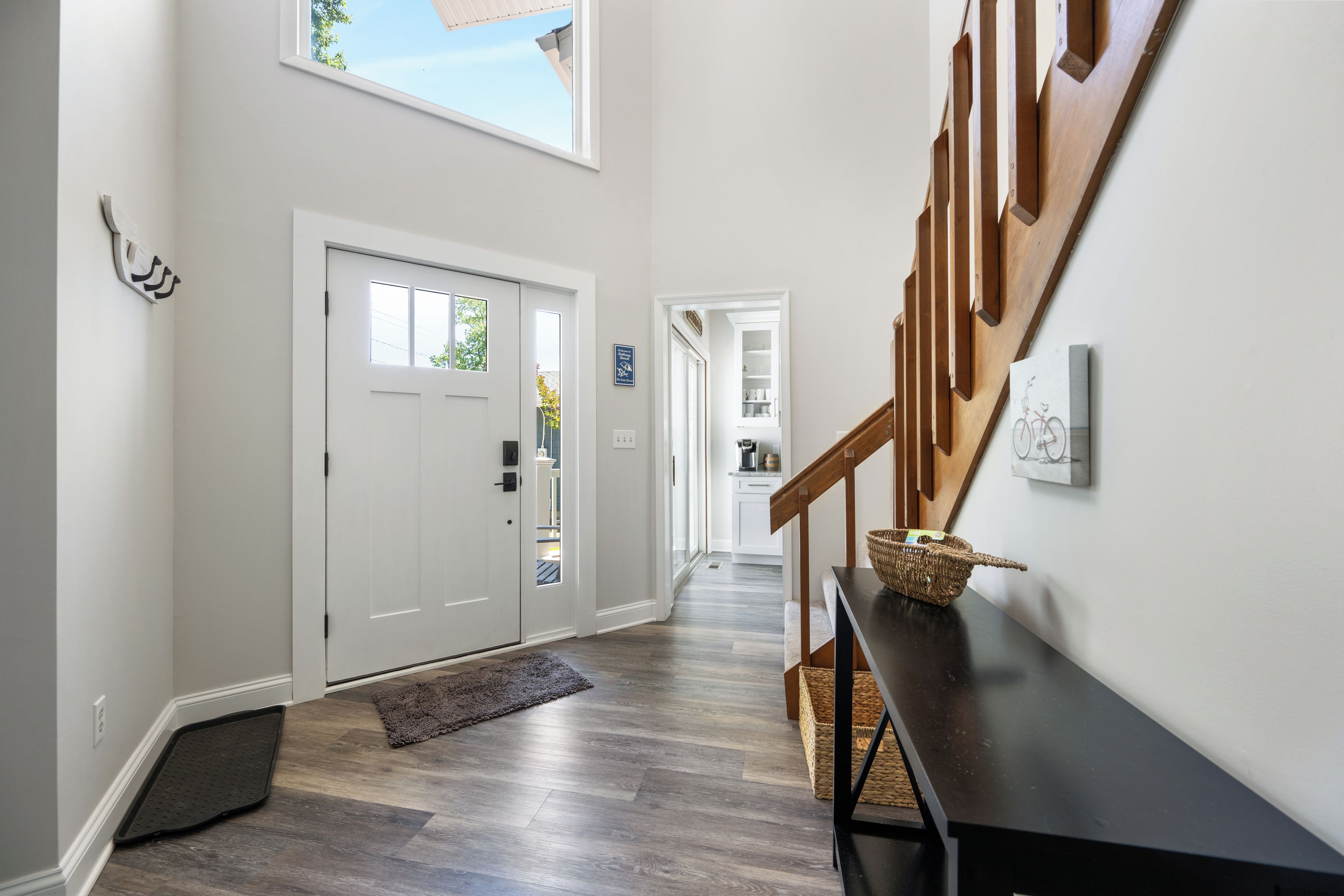 A hallway with a wooden staircase, a white door, and a view of a kitchen through an open door.