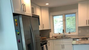 Una cucina moderna con mobili bianchi, un frigorifero in acciaio inossidabile, un forno integrato e una finestra che offre luce naturale.