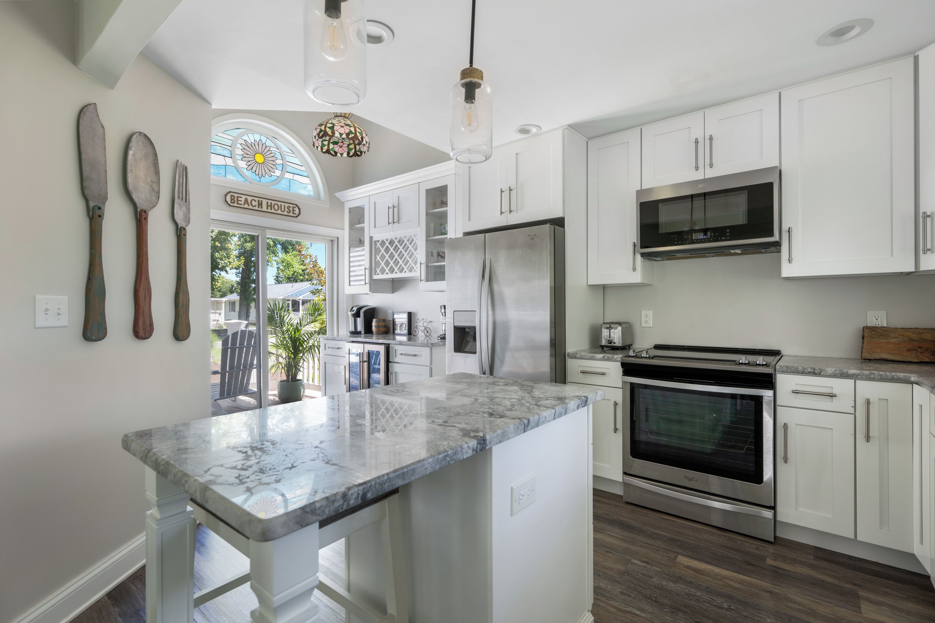 A modern kitchen with white cabinets, a stainless steel refrigerator, an oven, and a marble countertop.