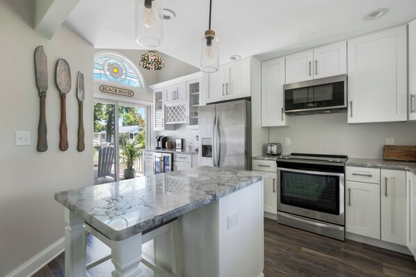 A modern kitchen with white cabinets, a stainless steel refrigerator, an oven, and a marble countertop.