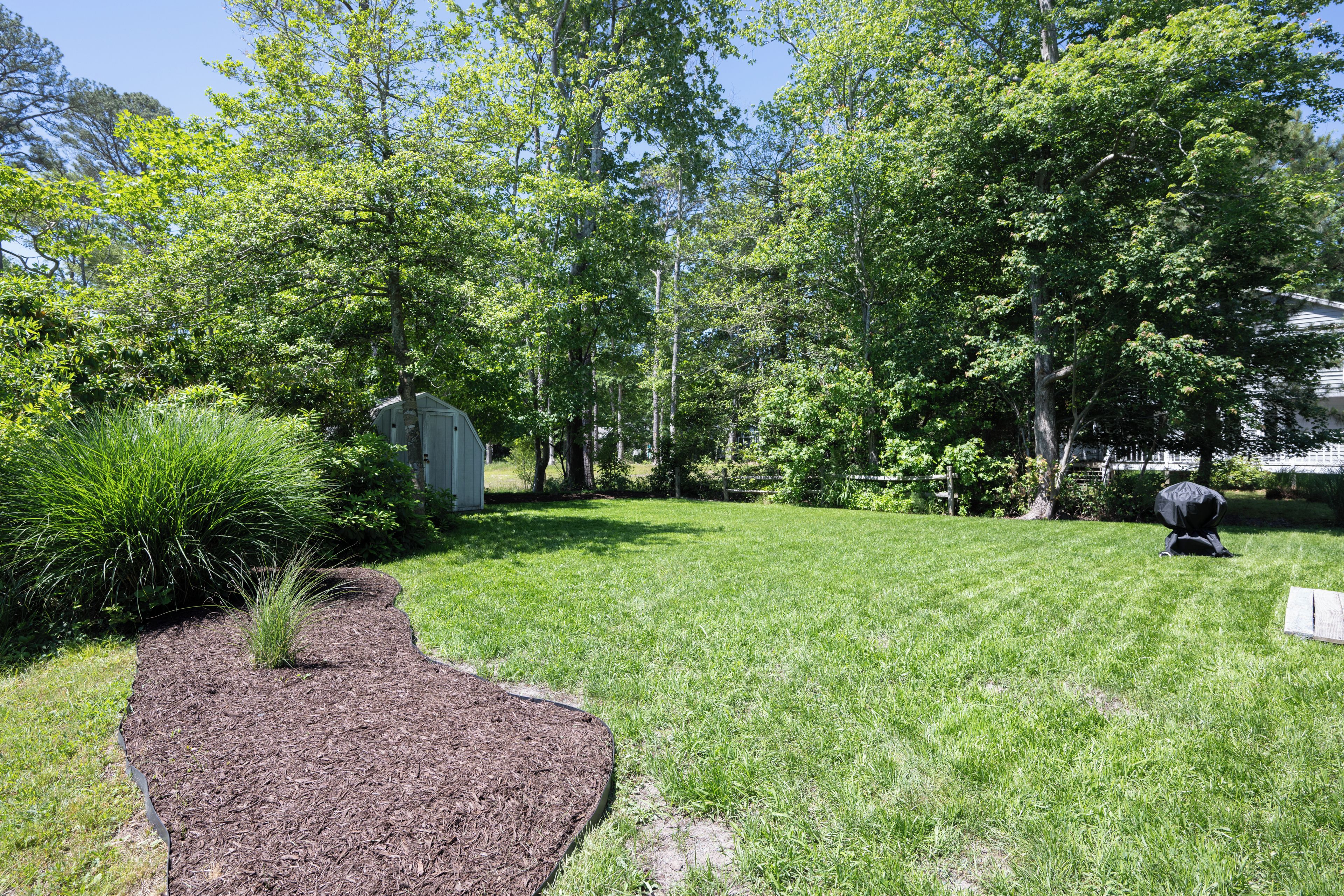 A well-maintained yard with a wooden deck, a barbecue grill, and a shed.