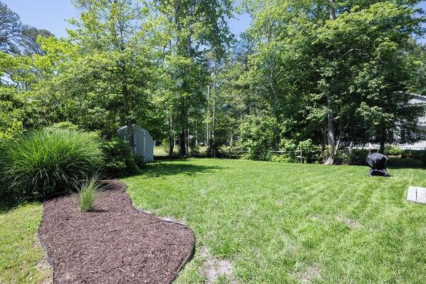 A well-maintained yard with a wooden deck, a barbecue grill, and a shed.