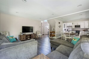 A spacious living room with a flat-screen TV, grey sofas, and a wooden entertainment unit.
