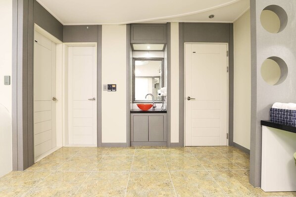 A hallway with two doors, a bathroom with a sink and mirror, and a tiled floor.
