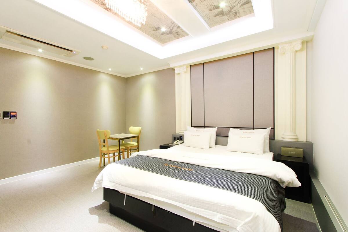 A modern hotel room with a large bed, a desk, and a chair.
