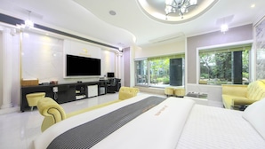 A spacious bedroom with a large bed, a flat-screen TV, a desk with a computer, and a seating area with chairs.