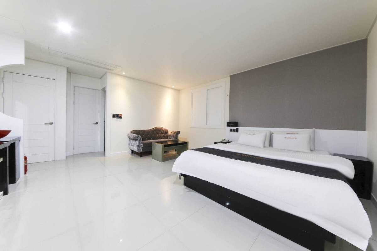 A modern hotel room with a large bed, a desk, and a sofa.