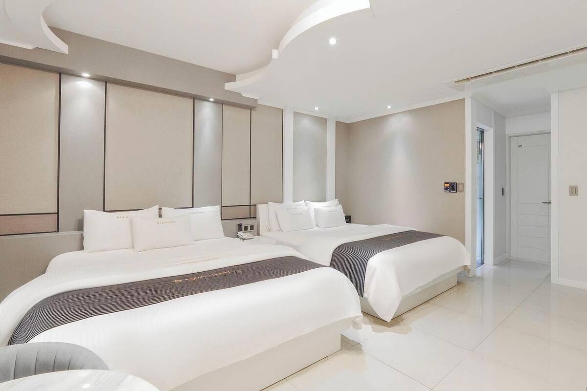 A modern hotel room with two beds, a large mirror, and a door leading to the hallway.