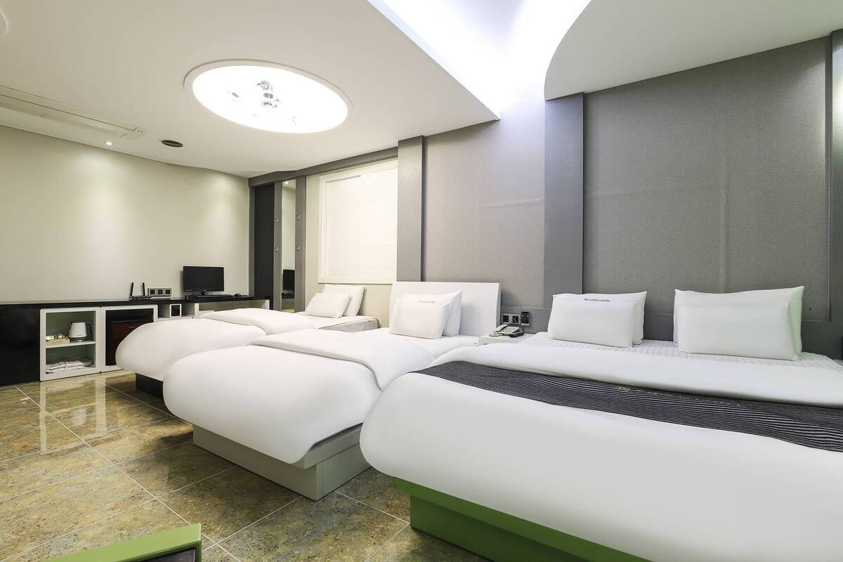 A modern hotel room with a large bed, a desk, a flat-screen TV, and a large window.