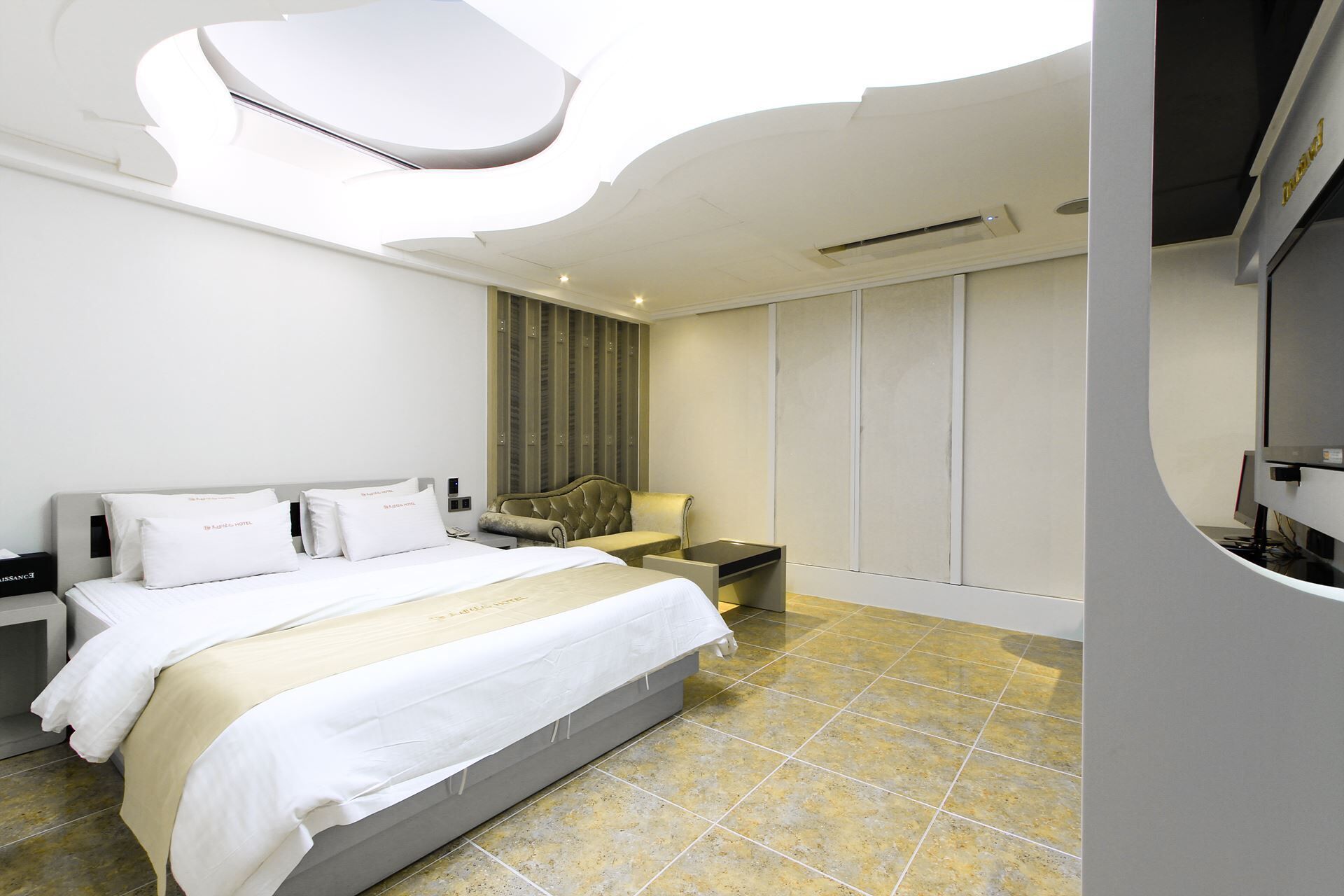 A modern hotel room with a bed, nightstands, a TV, and a wardrobe.